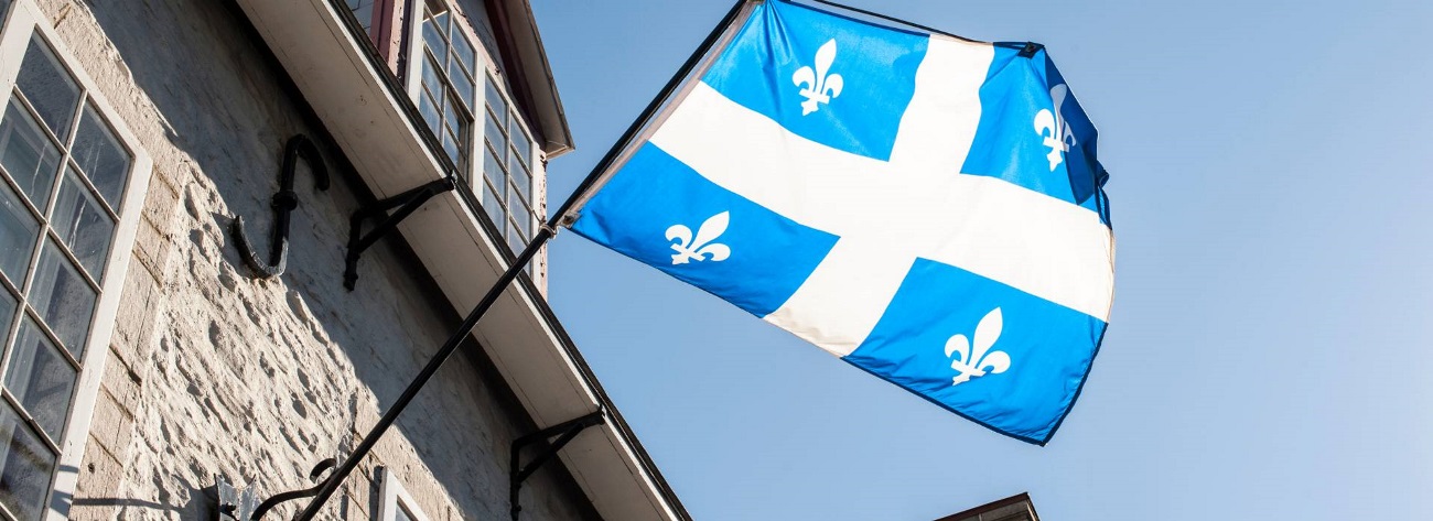 Quebec flag in front of a building - Link to [Webinar Replay] French Language Charter