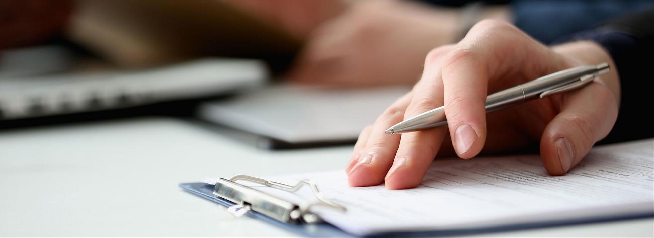 Hand of businessperson filling and signing a form with silver pen